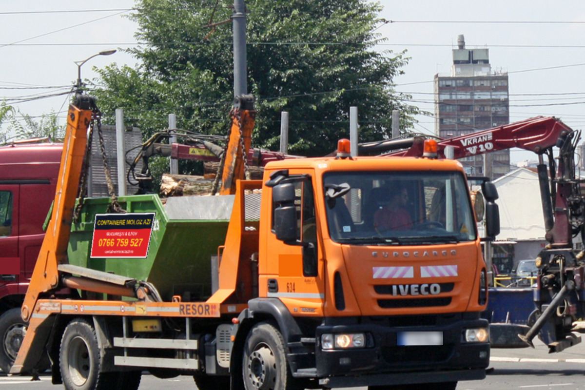 Autospecială cu brațe care încarcă un container de moloz verde, pe o stradă din București